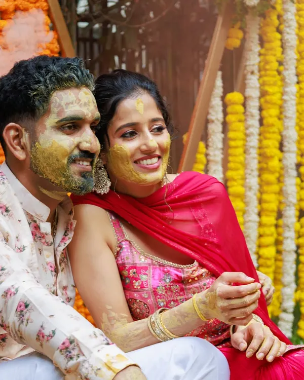A candid moment from a Haldi ceremony, full of smiles and laughter. The backdrop of traditional marigold garlands adds a burst of auspicious yellow, perfectly capturing the spirit of the event.