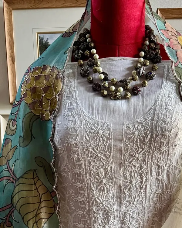 A classic off-white Chikankari suit is elevated by a stunning, hand-painted Srikalahasti Kalamkari organza dupatta. This image, styled with a necklace, shows the perfect harmony between the two crafts.