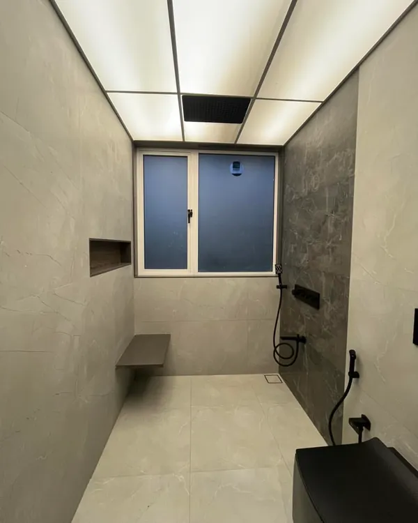 This modern bathroom in our Sanpada project features a stunning backlit stretch ceiling that provides even, diffused light. The floating bench and niche in the shower area add both style and practicality.