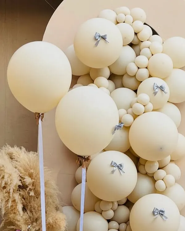 A close-up of our 'Babies in Bloom' boho decor, showing the delicate silver bow details on the cream-colored balloons and a hint of pampas grass.