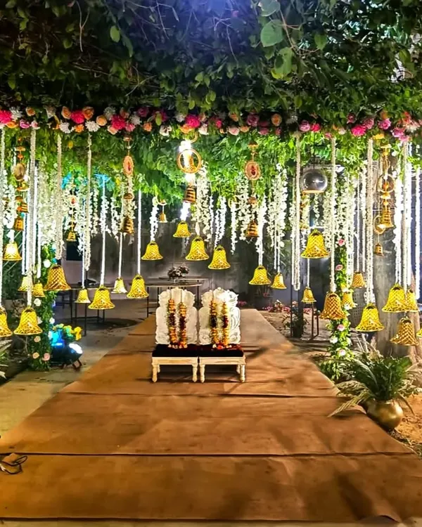 This nighttime wedding mandap was designed to feel like an enchanted forest. The structure is covered in natural greenery and flowers, with dozens of hanging floral strings and illuminated bells that cast a warm, magical glow over the ceremony.