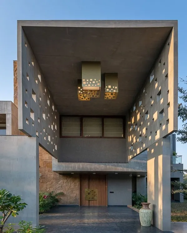 The entrance to this home is a study in Brutalist-inspired design. A massive concrete canopy with geometric cutouts creates a dramatic play of light and shadow, guiding you toward the warm wooden front door.