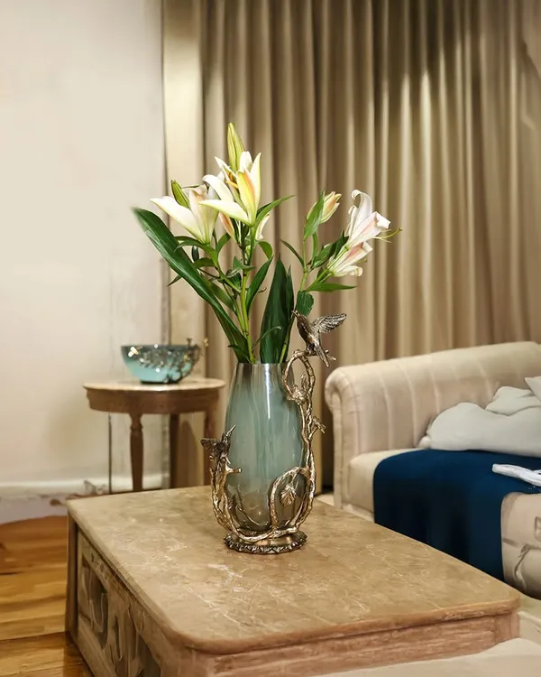A vase that does not just hold flowers, it holds stories. With sculpted birds dancing around hand-blown glass, this centerpiece brings art and nature together on your coffee table, creating a scene of whimsical elegance.