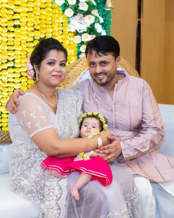 A beautiful family portrait taken during an Annaprasan ceremony. The parents are dressed in traditional wear, holding their baby girl, all smiling together.