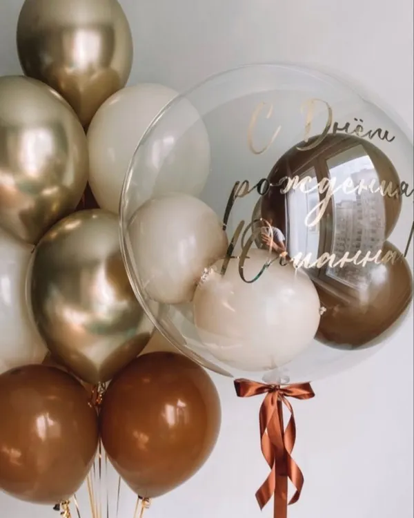 An elegant and sophisticated custom bubble balloon bouquet. This arrangement features a personalized clear bubble balloon filled with smaller balloons, surrounded by a bouquet in a chic palette of brown, beige, and chrome gold.