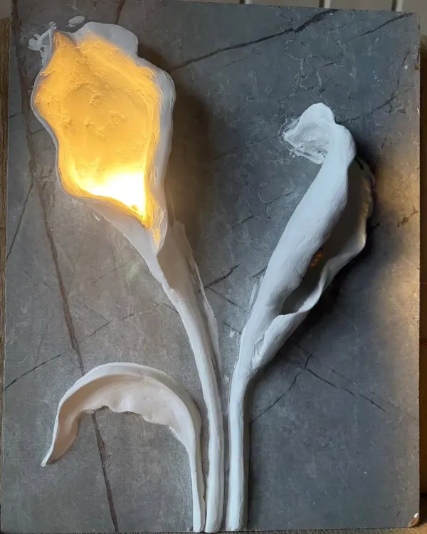 This 3D wall sculpture features calla lilies with a warm light glowing from within. Set against a grey marble-effect panel, the piece is both a work of art and an elegant light fixture.