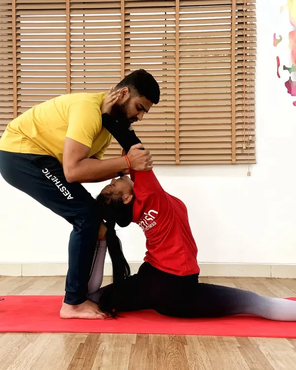 Assisting a student in a deep split pose, Hanumanasana, requires careful support to protect the muscles while encouraging greater flexibility.