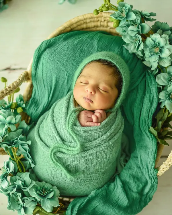 Perfectly posed with tiny hands tucked under the chin. This baby is swaddled in a lovely green wrap, surrounded by matching flowers for a cohesive and artistic newborn portrait.