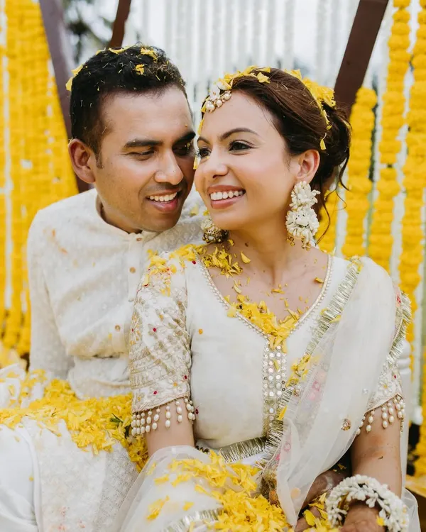 A sweet, candid moment of a couple during their Haldi, surrounded by marigold flowers, sharing a happy and intimate glance.