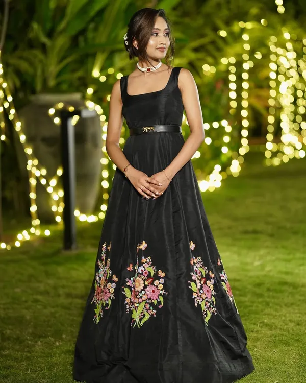 Actress Divya Shree from Australia in a custom-made black raw silk gown. The gown features a square neckline and is adorned with colorful floral hand embroidery at the hem.