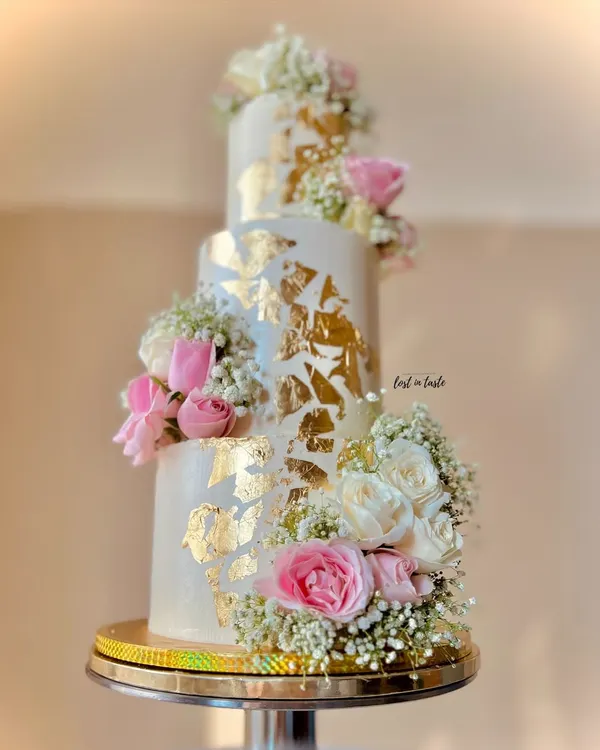 A beautiful three-tiered engagement cake with cascading fresh roses and baby's breath. The gold leaf accents and custom monogram add a touch of personalized luxury.