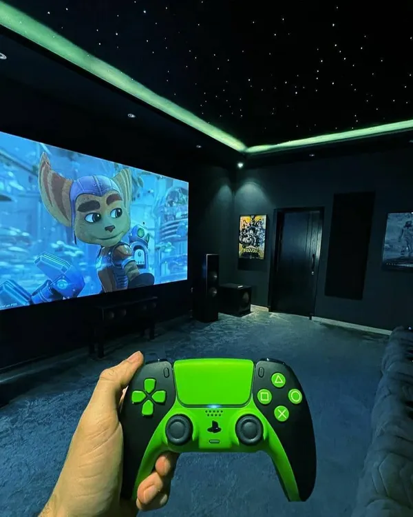A first-person view of a gaming session in a custom-built room. The setup includes a massive screen, tower speakers, and a fiber-optic starfield ceiling to create a completely immersive environment.