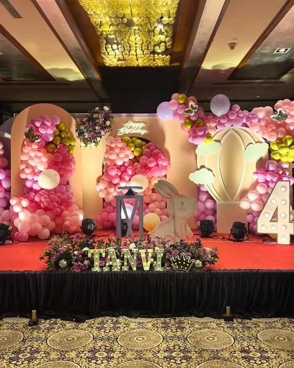 A breathtaking butterfly and bunny themed stage for a fourth birthday. The grand setup includes multiple backdrops, massive pink balloon displays, floral arrangements, and large rabbit figures.