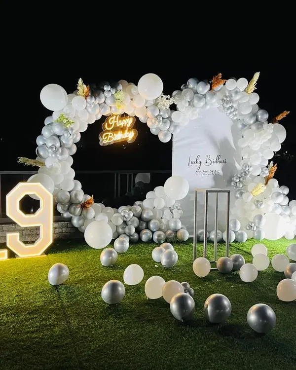 For this 19th birthday, I created a stylish heart-shaped balloon arch in white and silver on a green lawn. The large, lit-up marquee numbers and scattered balloons made for a perfect photo spot for this outdoor terrace party.