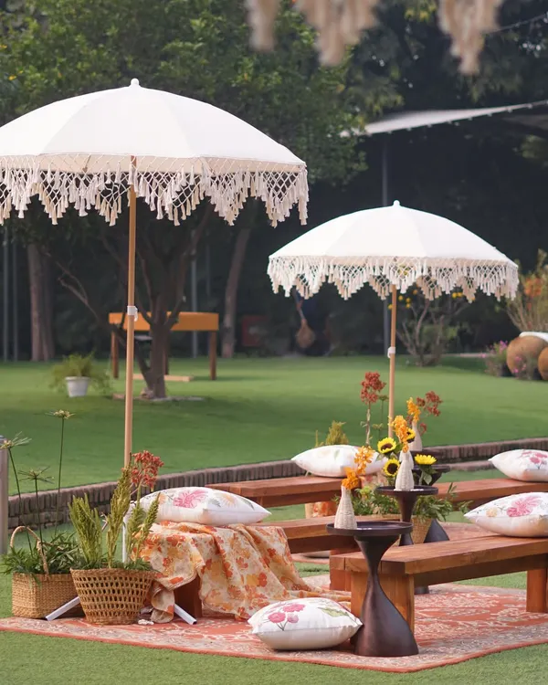 A perfect picnic-style setup for a Mehendi. The combination of rustic benches, bohemian umbrellas, and colorful textiles creates a relaxed and chic vibe.