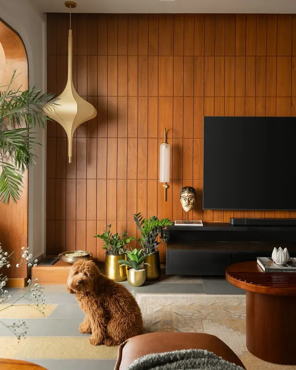 In this home inspired by Indian heritage, the living area features a teak veneer wall with brass accents as a warm backdrop. The space is grounded by a fusion of polished and unpolished Kota stone flooring with Jaisalmer marble inlays.