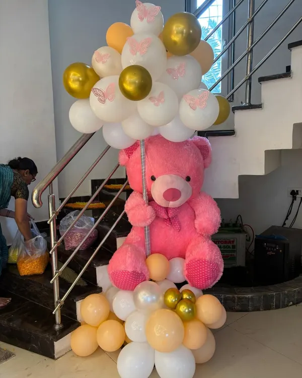 A cute welcome prop for a butterfly-themed party, featuring a large pink teddy bear holding a bunch of balloons with butterfly prints.