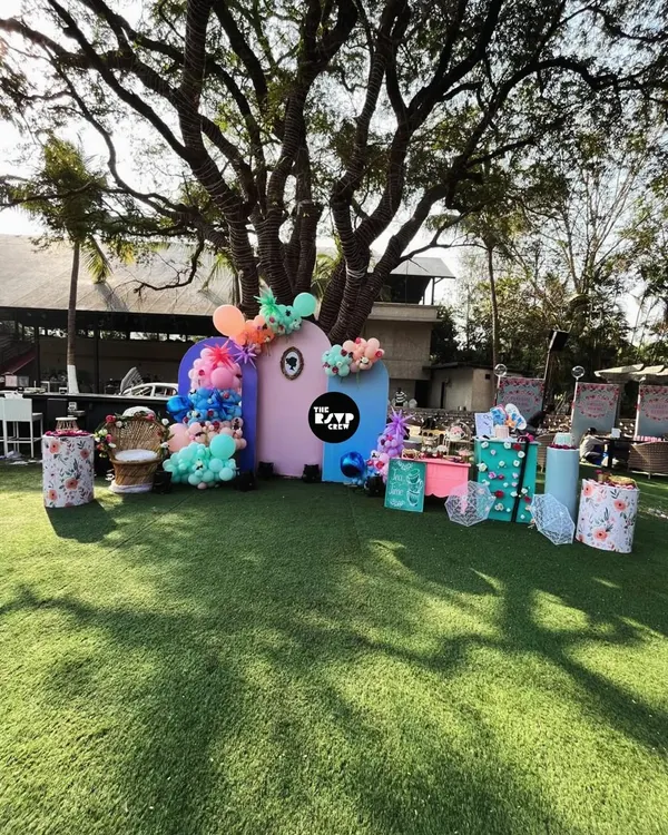 For this outdoor baby shower, we created a fun and colorful backdrop on a lush green lawn. The setup features abstract pastel panels, vibrant balloon clusters, and a dedicated dessert table, all centered around a large tree for a playful, natural feel.