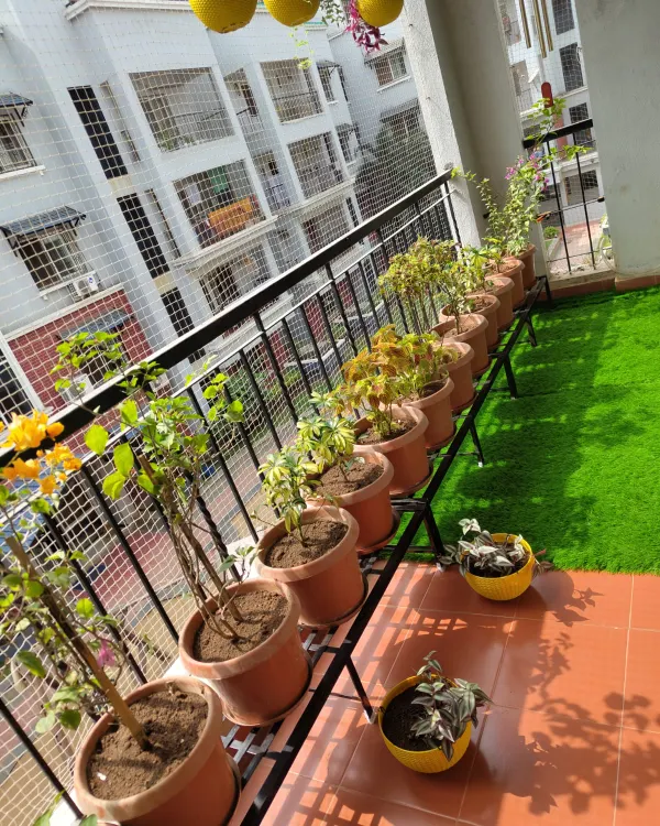 A perfect example of a functional and beautiful apartment balcony. The design uses artificial grass for easy upkeep, planters on stands to maximize floor space, and a full-coverage safety net, making it a safe and green spot to relax.