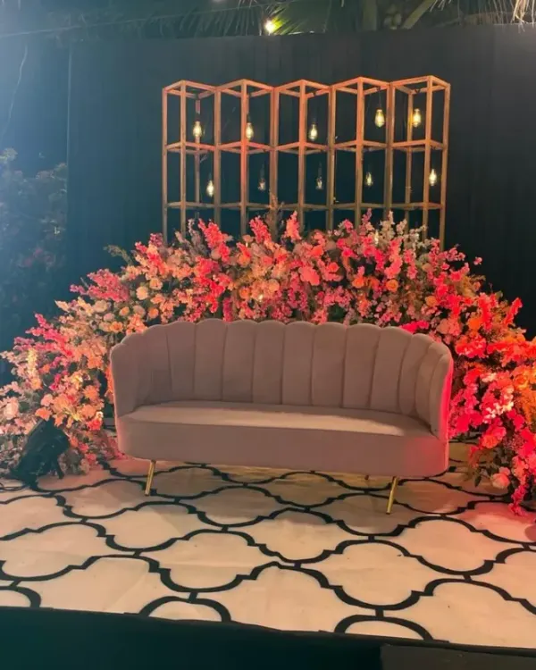 A chic and modern photo booth for a reception. We combined a plush velvet sofa with a backdrop of lush flowers and a geometric gold shelf, creating a stylish spot for guests to take pictures.