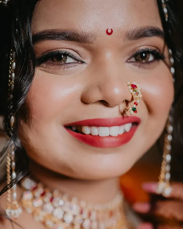 A close-up of this stunning Maharashtrian bride. Her radiant smile, classic red lip, and traditional jewelry come together for a breathtaking look. The airbrush makeup ensures a flawless finish.