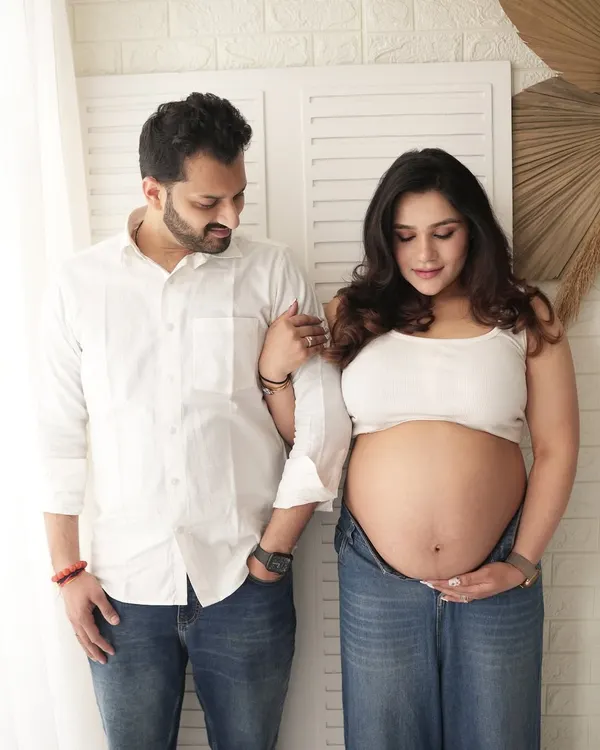 A relaxed and modern couple's portrait. The casual white tops and jeans create a comfortable and authentic feel for this studio maternity shoot.