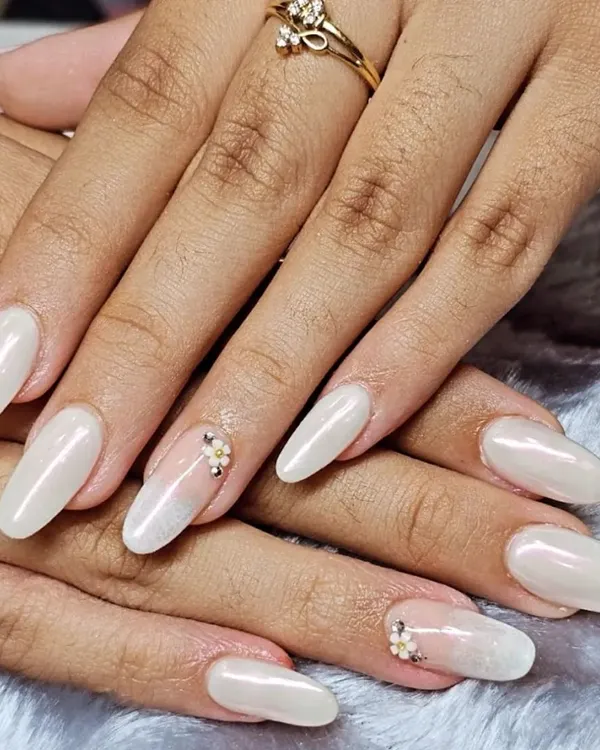 This elegant look features almond-shaped nail extensions with a pearly white chrome finish. A delicate, hand-placed floral rhinestone cluster on the accent nail adds a touch of sparkle.