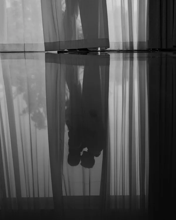 A stolen moment behind the curtains. This artistic reflection shot captures the couple in a quiet, intimate embrace before the whirlwind of the day begins, a secret memory just for them.