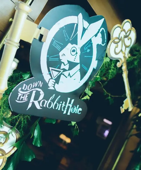 The adventure begins here. This "Down the Rabbit Hole" sign, complete with a White Rabbit graphic and overgrown ivy, serves as the perfect entrance to our whimsical Alice in Wonderland themed brunch.