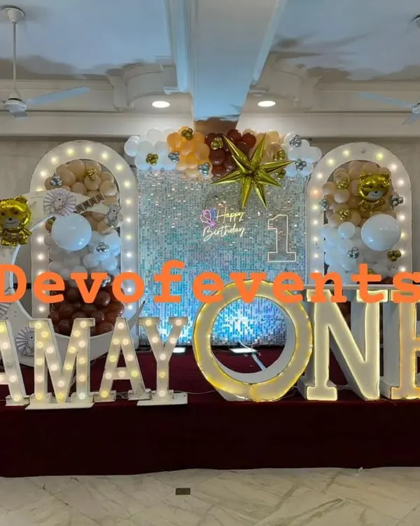 A grand stage for a teddy bear themed first birthday. This setup features a silver sequin shimmer wall, large light-up marquee letters for the name and age, and balloon arrangements in white, brown, and gold.