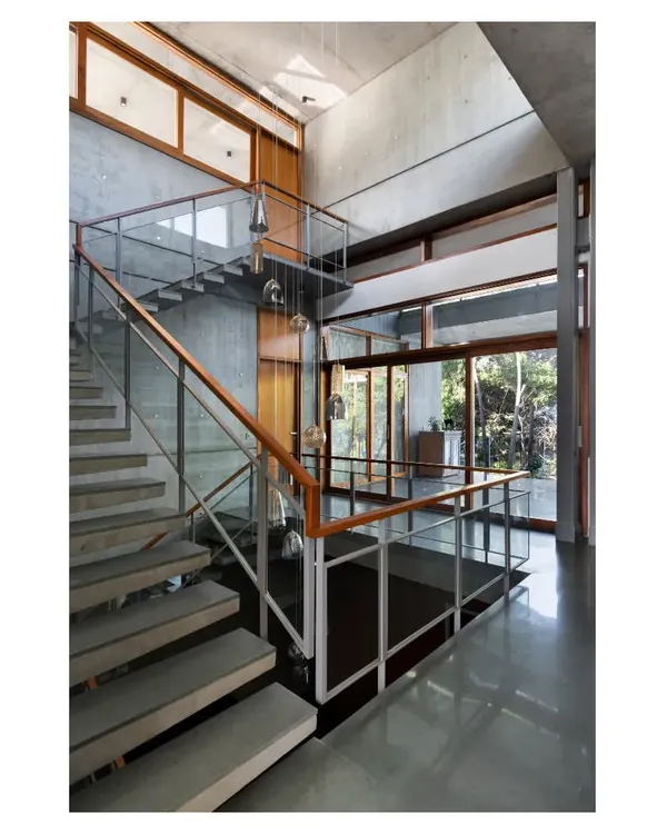 The cantilevered concrete staircase in the 'House of Canopies' is a feat of engineering and a central sculptural element. It appears to float against the raw concrete walls, connecting the different levels of the triple-height space.