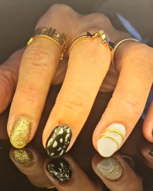 A chic and contrasting manicure featuring gold glitter, black and white patterns, and gold striped accents.