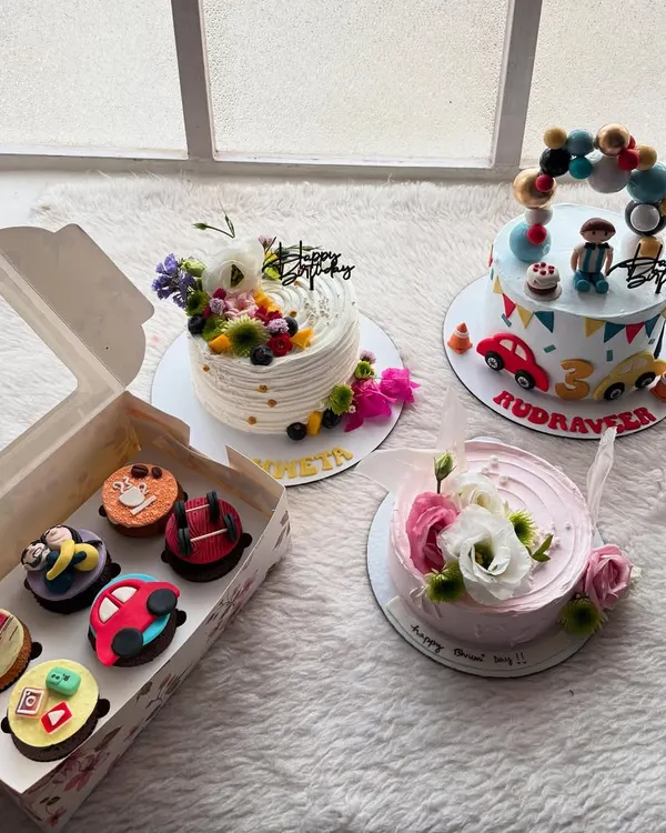 This picture captures a typical busy day in my kitchen. It shows the variety I love to create, including a custom car-themed birthday cake, a delicate floral bento cake, and a box of assorted fondant cupcakes for a special celebration.