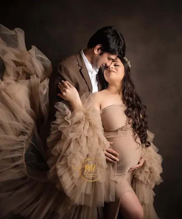An intimate moment between an expecting couple. The flowing fabric of the gown adds a touch of drama and elegance to this maternity portrait against a classic dark backdrop.
