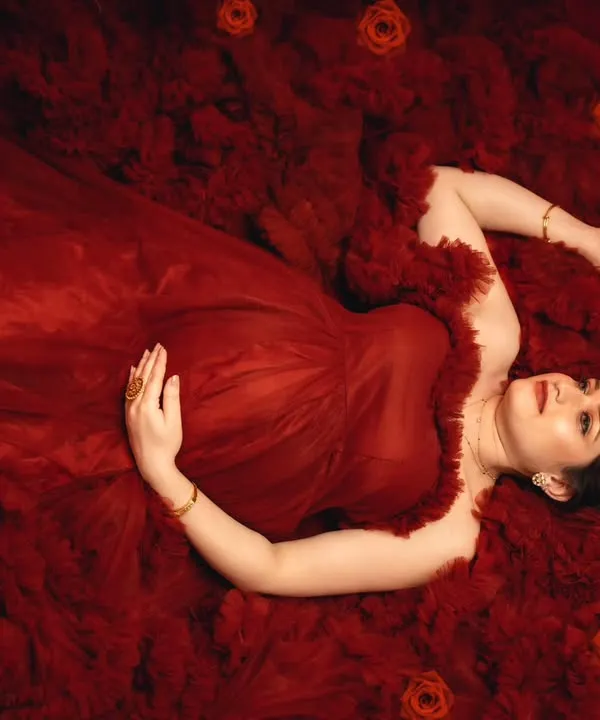 A breathtaking overhead shot of a mother-to-be lying in a sea of red tulle, creating an artistic and romantic vision of motherhood.