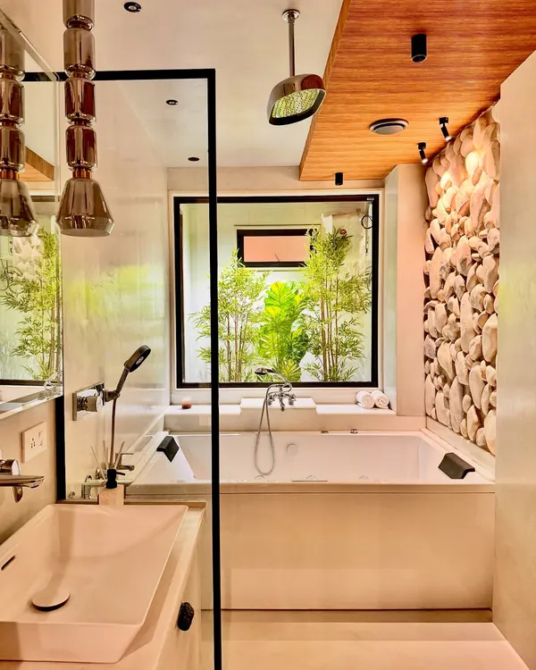 In this biophilic bathroom design, I wanted to blur the line between inside and out. A large window looks out onto a private bamboo garden, bringing a sense of nature directly into the space. The design features a jacuzzi bathtub, a pebble-stone accent wall, and a wooden ceiling to create a complete sensory experience of a luxury home spa.