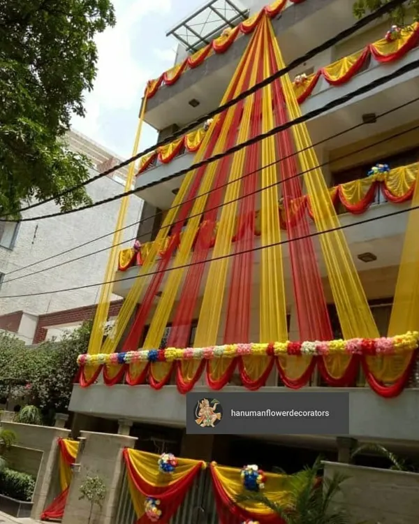 I make sure the festive feeling starts right at the entrance. This is an exterior decoration for a multi-story residence, using bright yellow and red drapes and floral arrangements to make the entire building look ready for a celebration.