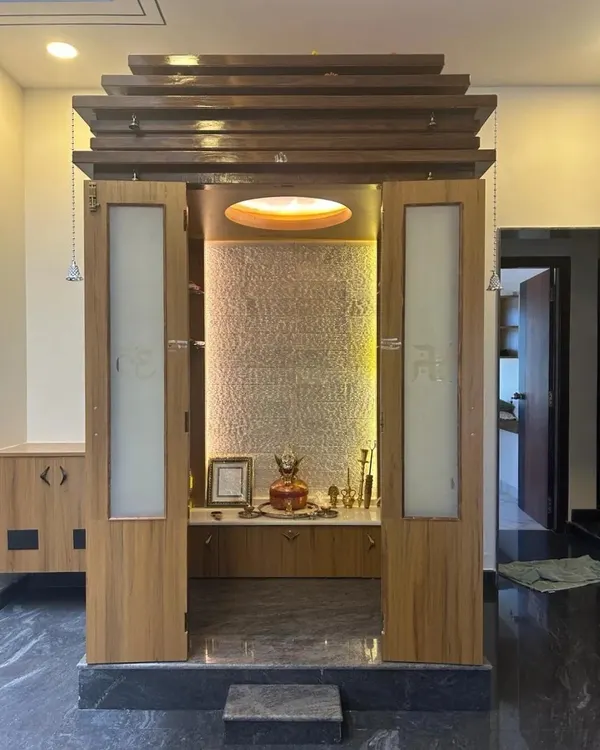 This modern pooja unit is designed to be a spiritual centerpiece in a contemporary home. It features a beautiful textured backdrop, soft lighting, and elegant frosted glass doors with Swastik symbols.