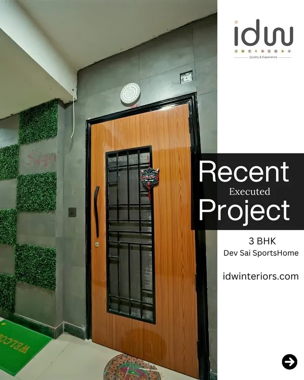 A modern entrance at Dev Sai SportsHome. The door features a wood finish with a metal grill, complemented by a concrete-texture wall and artificial green panels for a unique look.