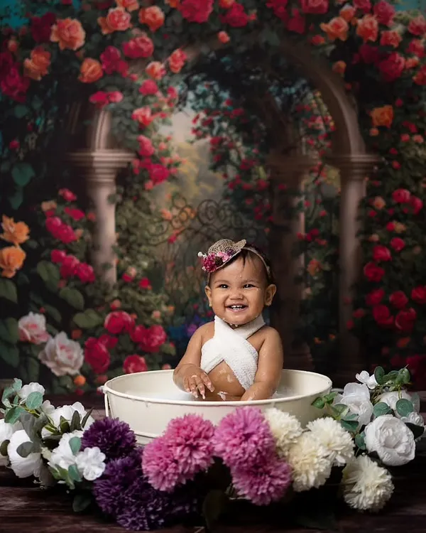 A huge, happy grin from this baby during her floral milk bath session. The tub is surrounded by beautiful flowers, creating a whimsical garden feel.