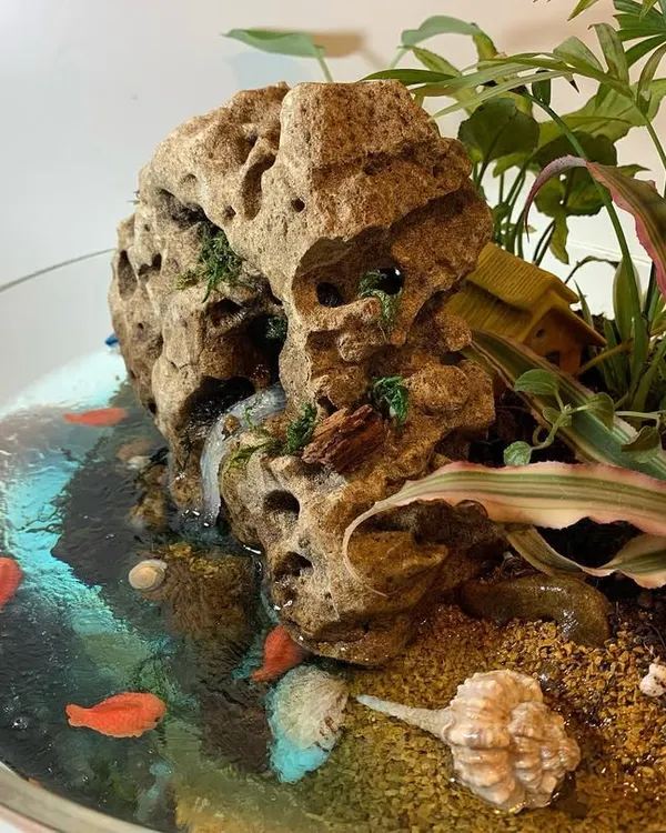 This is one of my favorite creations, a miniature beach scene in a glass bowl. I used resin to craft a realistic water effect around a porous rock waterfall, adding real seashells and tiny fish figures to complete the coastal landscape. The surrounding tropical plants, like the small palm and bromeliad, are low maintenance and bring the whole scene to life.
