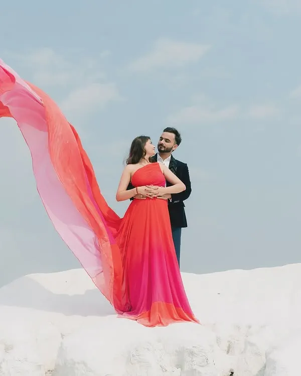 A dramatic pre-wedding portrait session featuring a vibrant, flowing gown against a minimalist landscape. This kind of cinematic shot is perfect for creating epic, magazine-worthy images that tell a grand love story.