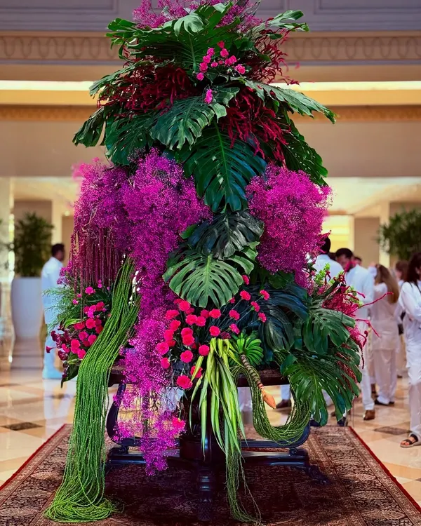 A symphony of pink and green. This large-scale lobby arrangement combines lush monstera leaves with vibrant pink orchids and cascading foliage to create a tropical yet elegant statement piece.