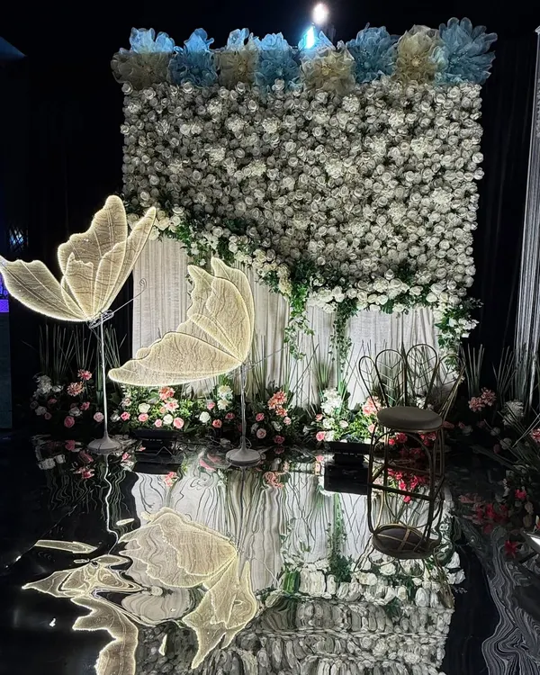 A whimsical and dreamy photo booth. We created this with a wall of white flowers, glowing butterfly installations, and a reflective floor for a magical effect.