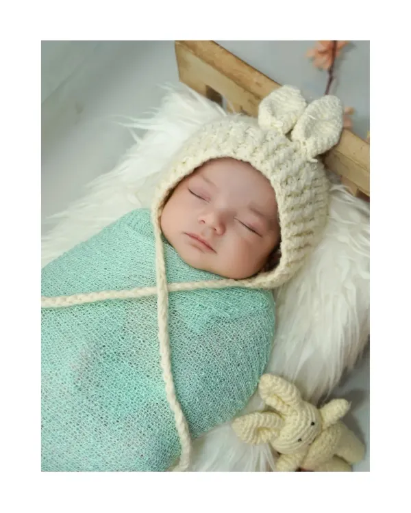 A peaceful close up of a sleeping newborn. I use soft wraps and adorable props like this knit bunny hat to create sweet, serene images of your baby.