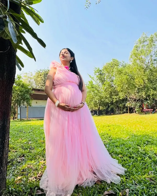 A beautiful solo portrait taken in a garden setting. The natural sunlight and green background make this pink maternity gown look even more vibrant and beautiful.