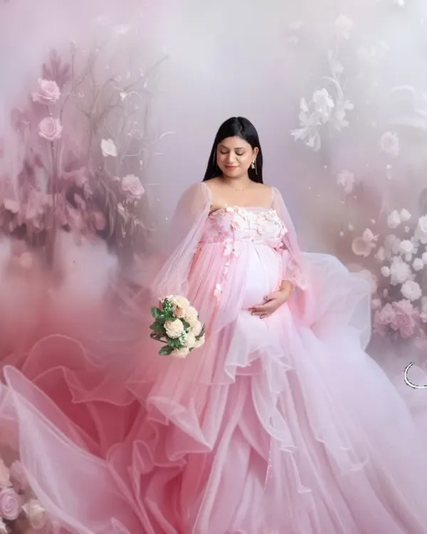 A dreamy, ethereal portrait of a mother-to-be in a flowing pink gown, surrounded by a magical fog and floral arrangement. This is a perfect example of a fantasy-style fine art shoot.