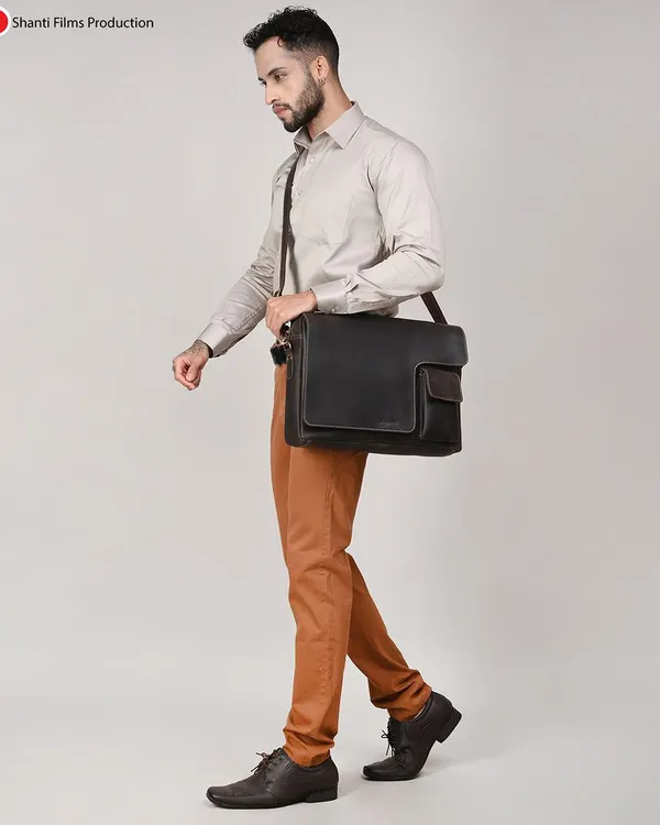 This lifestyle shot showcases a men's leather messenger bag in a professional context. The walking pose demonstrates the bag's size and how it's worn, helping customers gauge its practicality.