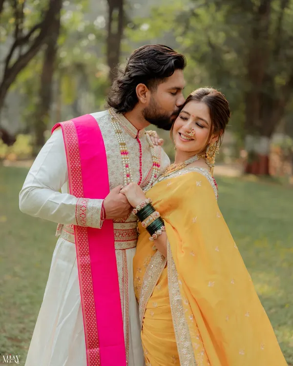 A gentle kiss on the forehead captures the tenderness of this couple's bond. This close-up highlights the groom's traditional attire and the bride's joyful expression during their outdoor Marathi-themed pre-wedding shoot.