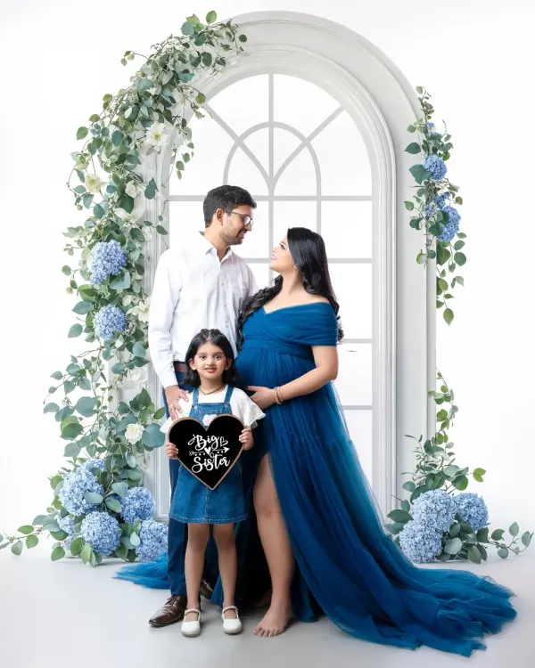 The whole family is excited to meet their new "Brother & Bestie." This beautiful portrait is framed by a stunning floral arch, with the older sister proudly holding a sign to celebrate her new role.